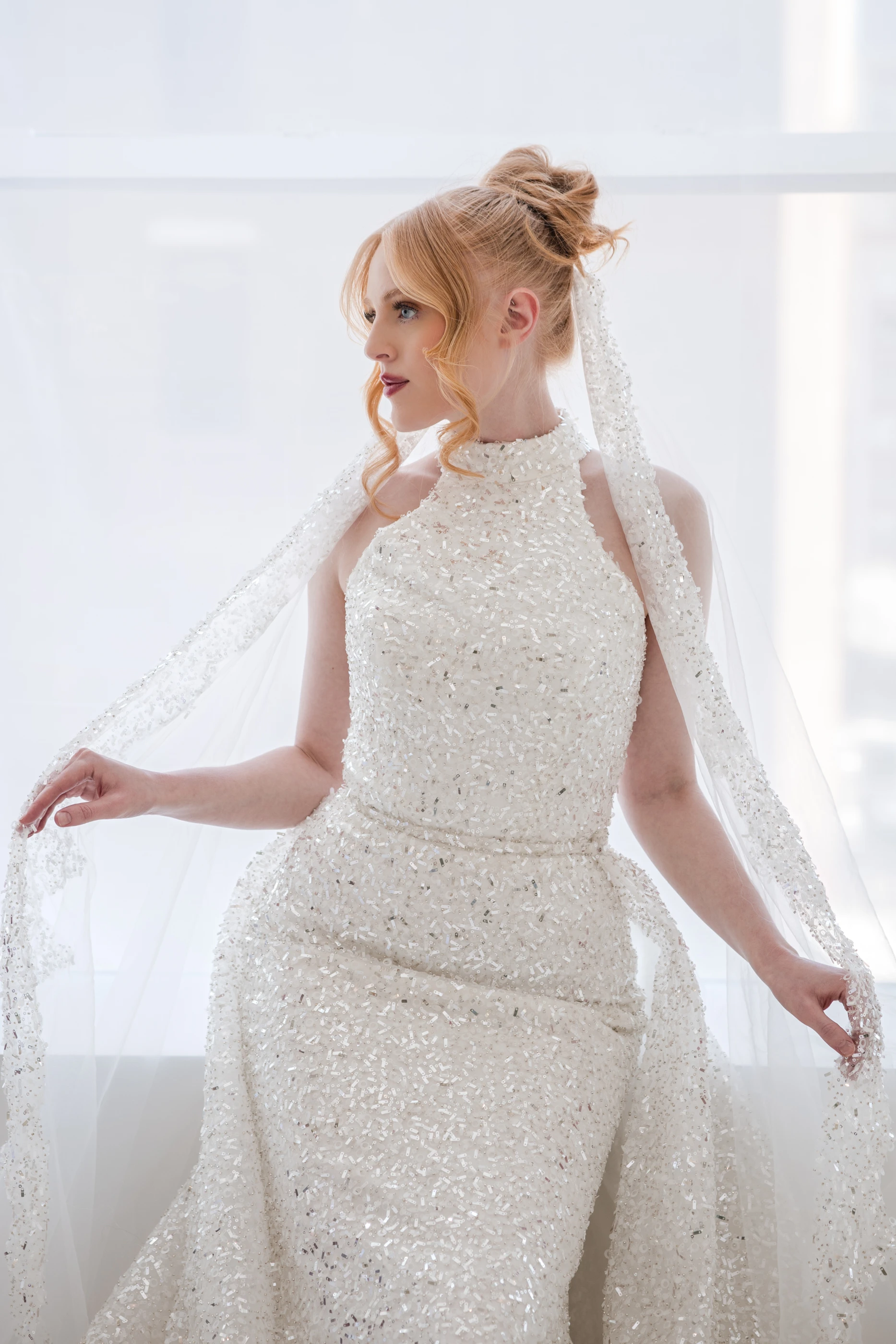 Bride in the Candace gown and veil beside a bright window